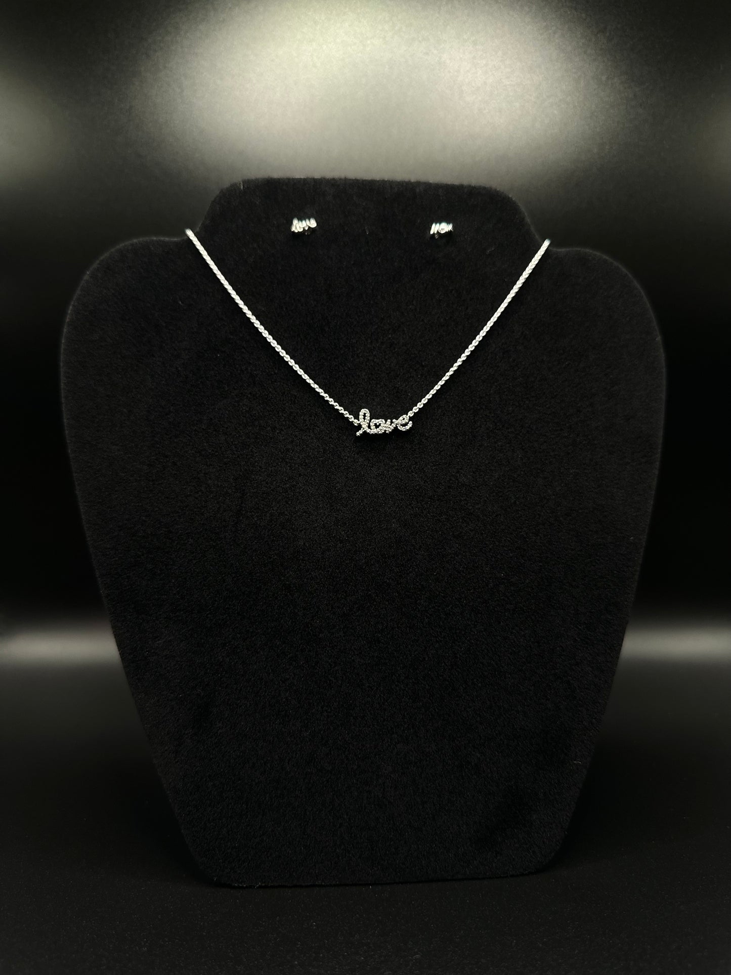 Necklace with 'love' pendant on a black stand against a dark background